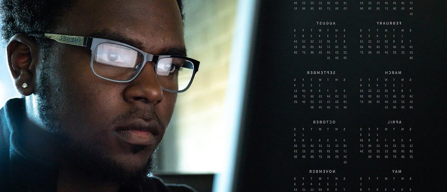 A male student looking at a screen with a monthly calendar.